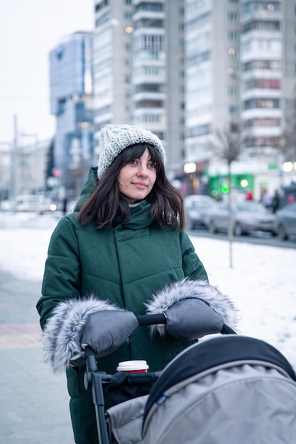 Elegante joven madre a pasear con su bebé en un cochecito de bebé en invierno