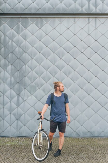 Elegante joven con mochila de pie con su bicicleta