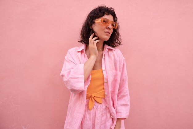 Elegante joven morena caucásica con gafas, ropa de verano, mira hacia otro lado, pasa tiempo con fondo rosa