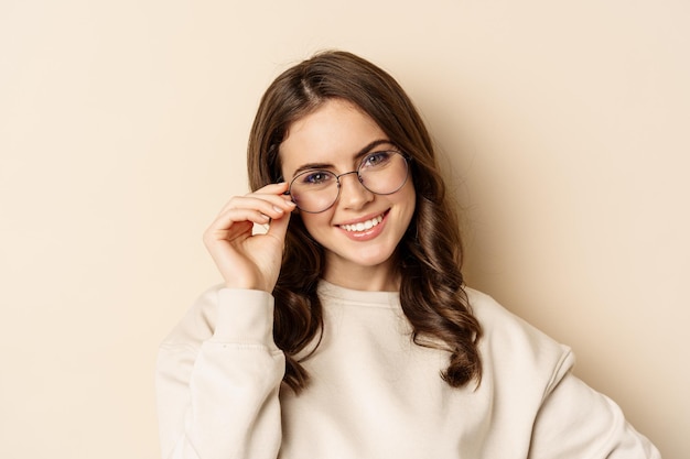 Elegante joven mujer caucásica con gafas y sonriendo, posando sobre fondo beige. copia espacio