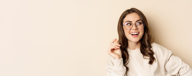 Foto gratuita elegante joven mujer caucásica con gafas y sonriendo posando sobre fondo beige