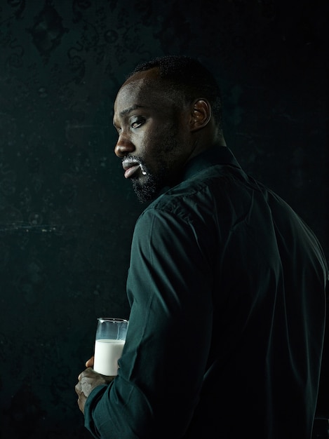 Elegante joven negro africano con taza de café blanca posando sobre fondo oscuro de estudio.