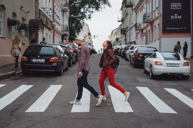 Elegante joven pareja posando al aire libre. Un hombre joven con una cerda en un casquillo con una muchacha con el pelo largo. Los jóvenes felices caminan por la ciudad. retrato. de cerca.