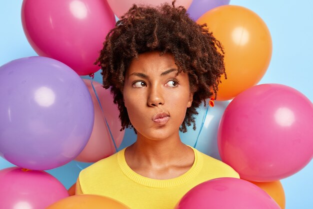Elegante joven pensativa posando rodeada de globos de colores de cumpleaños