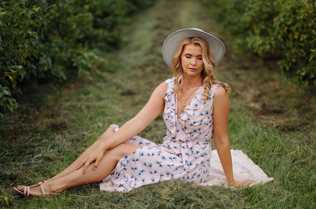 Elegante joven en rosa vintage azul vestido y sombrero posando en campo verde