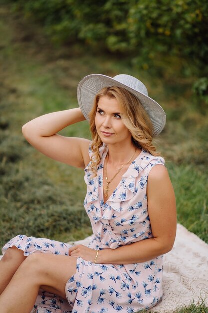 Elegante joven en rosa vintage azul vestido y sombrero posando en campo verde