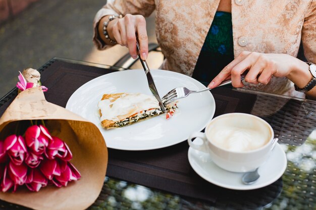 Elegante joven sentado en la cafetería, comiendo pastel sabroso