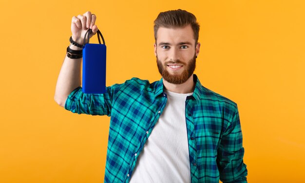 Elegante joven sonriente sosteniendo altavoz inalámbrico escuchando música en naranja