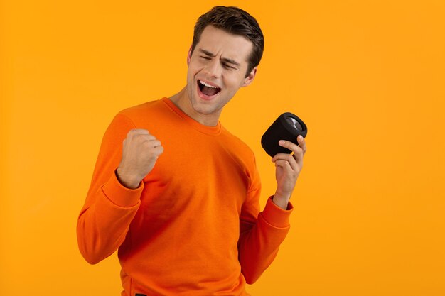 Elegante joven sonriente en suéter naranja con altavoz inalámbrico feliz escuchando música divirtiéndose en naranja