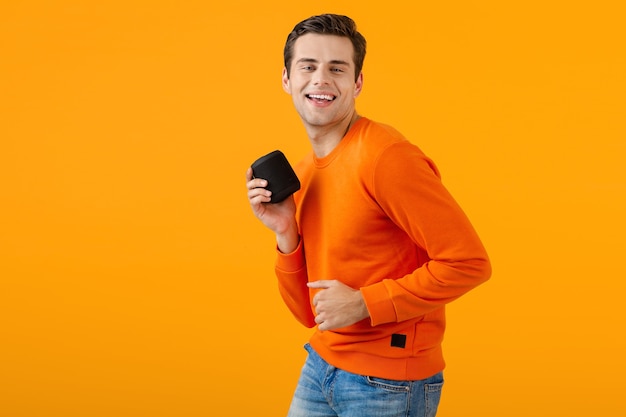 Elegante joven sonriente en suéter naranja con altavoz inalámbrico feliz escuchando música divirtiéndose