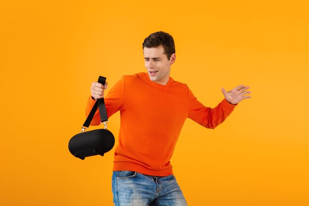 Elegante joven sonriente en suéter naranja con altavoz inalámbrico feliz escuchando música divirtiéndose