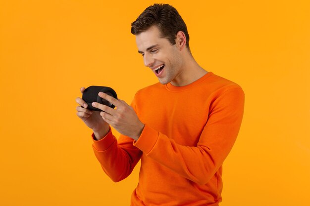 Elegante joven sonriente en suéter naranja con altavoz inalámbrico feliz escuchando música