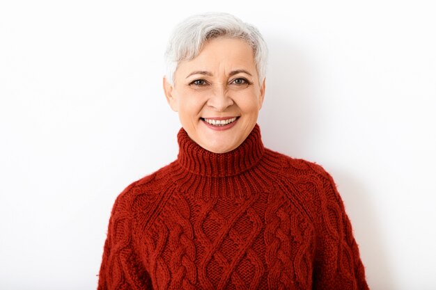 Elegante jubilada mujer caucásica alegre con peinado de duendecillo corto sonriendo ampliamente, vestida con un elegante jersey de punto burdeos. Personas, edad, estilo, prendas de punto y concepto de moda.