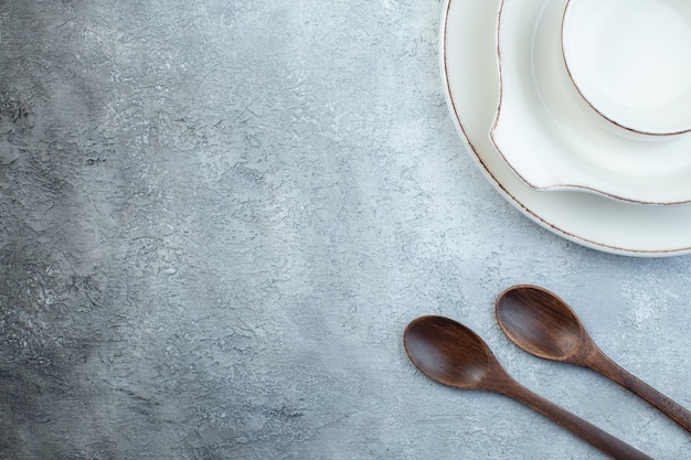 Foto gratuita elegante juego blanco vacío para la cena y cucharas de madera en el lado izquierdo sobre una superficie gris aislada con espacio libre