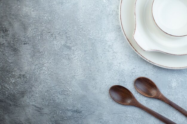 Elegante juego blanco vacío para la cena y cucharas de madera en el lado izquierdo sobre una superficie gris aislada con espacio libre