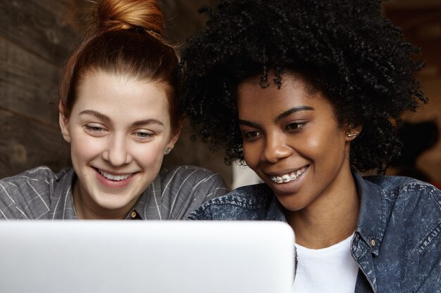 Elegante lesbiana negra con peinado afro y tirantes navegando por internet o comprando en línea