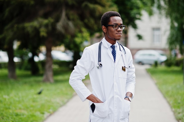 Elegante médico afroamericano con estetoscopio y bata de laboratorio en gafas posadas al aire libre