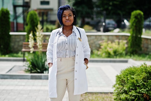 Elegante médico afroamericano con estetoscopio y bata de laboratorio posada en el patio trasero del hospital