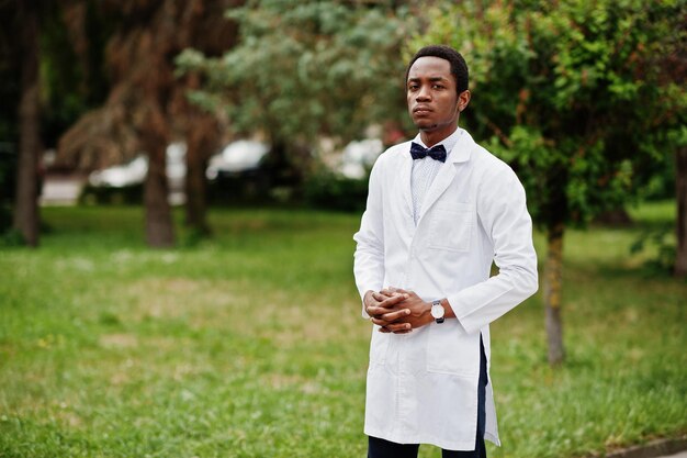 Elegante médico afroamericano con pajarita y bata de laboratorio posada al aire libre