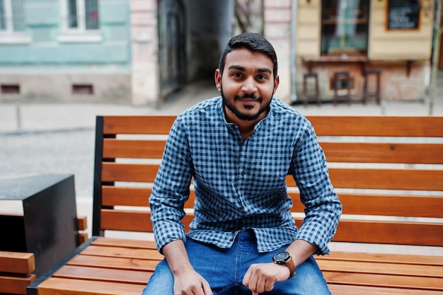 Elegante modelo de barba india con ropa informal posó al aire libre sentado  en un banco en la calle de la india y mirando sus relojes