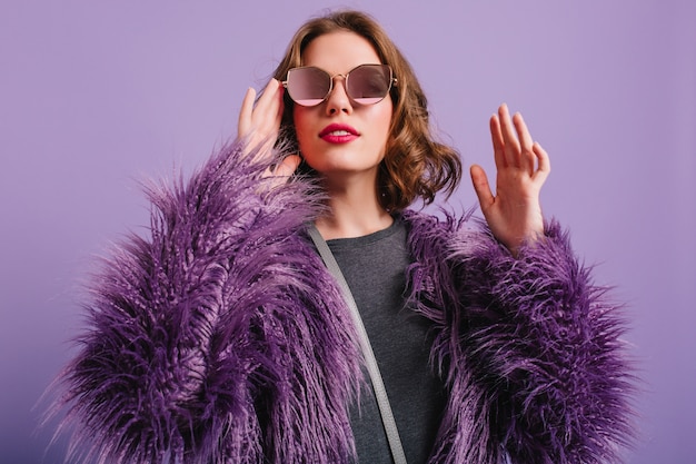 Elegante modelo femenino europeo posando sobre fondo morado con sonrisa complacida