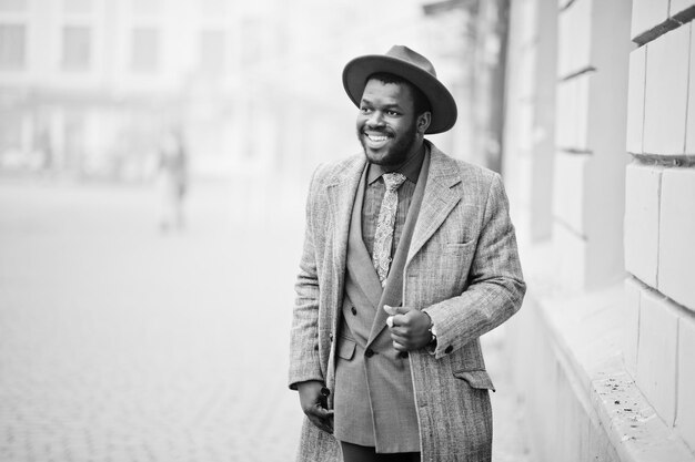 Elegante modelo de hombre afroamericano con chaqueta de abrigo gris, corbata y sombrero rojo Foto en blanco y negro