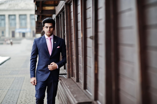 Elegante modelo de hombre macho indio con traje y corbata rosa posado contra puestos de madera