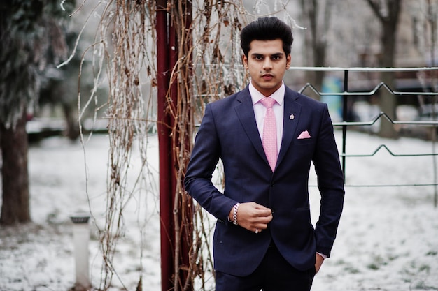 Elegante modelo de hombre macho indio con traje y corbata rosa posado en el día de invierno