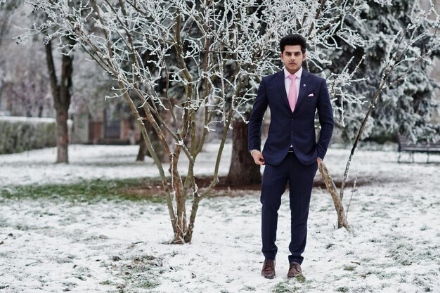 Elegante modelo de hombre macho indio con traje y corbata rosa posado en el día de invierno