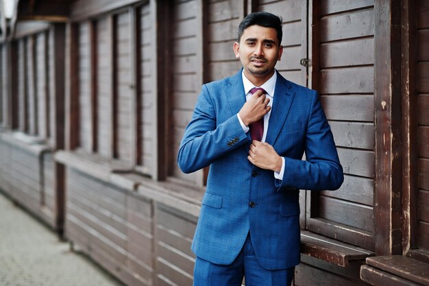 Elegante modelo de hombre de moda indio en traje posado contra puestos de madera