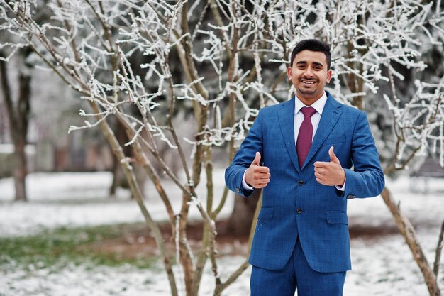 Elegante modelo de hombre de moda indio en traje posado en el día de invierno muestra los pulgares hacia arriba