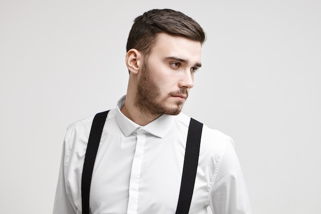 Foto gratuita elegante modelo masculino joven con barba de tres días recortada y corte de pelo posando para publicidad de ropa o peluquería, mirando hacia los lados con expresión seria pensativa. gente, belleza, estilo y moda