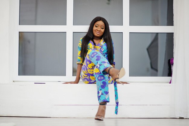 Elegante modelo de mujer afroamericana vestida con ropa de colores Mujeres afro elegantes en la habitación contra la ventana en la noche