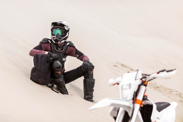 Elegante motociclista relajante en el desierto