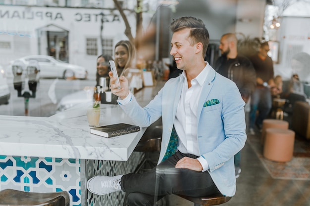 Elegante muchacho sentado en un bar chateando en el móvil