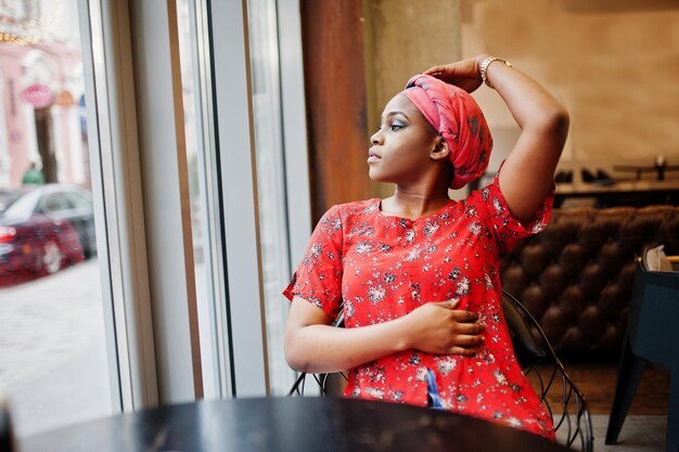 Elegante mujer africana con camisa roja y sombrero posó en un café interior