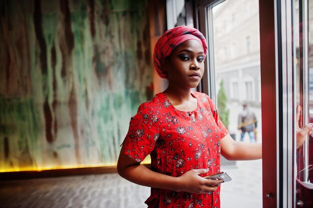 Elegante mujer africana con camisa roja y sombrero posó en un café interior