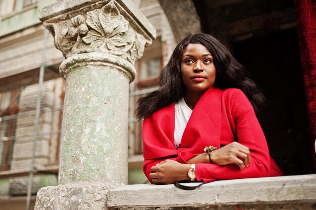 Elegante mujer afroamericana con abrigo rojo posada contra columnas antiguas