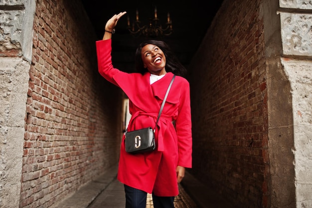 Elegante mujer afroamericana en abrigo rojo posó en tonel al aire libre