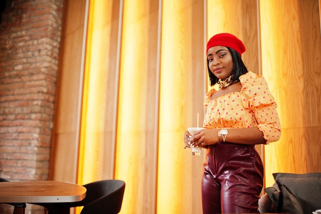 Foto gratuita elegante mujer afroamericana en boina francesa roja blusa de lunares con cadena de cuello dorado grande y pantalones de cuero pose interior