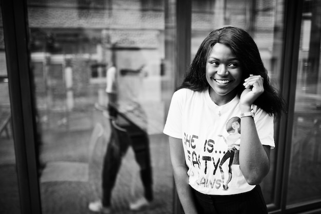 Elegante mujer afroamericana en camiseta impresa posada al aire libre contra la ventana