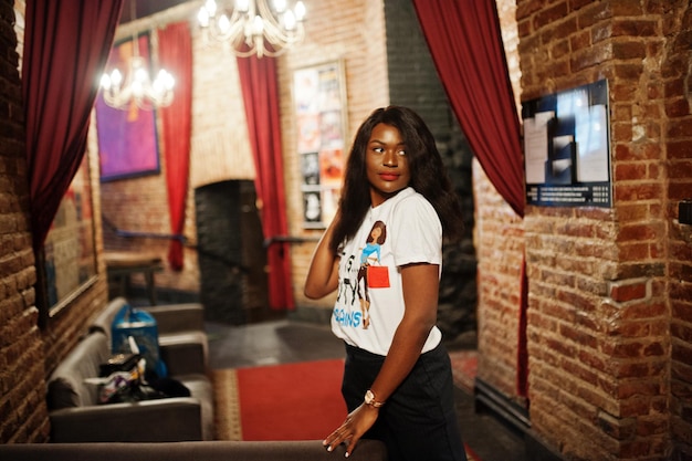 Elegante mujer afroamericana en camiseta impresa posada en interiores