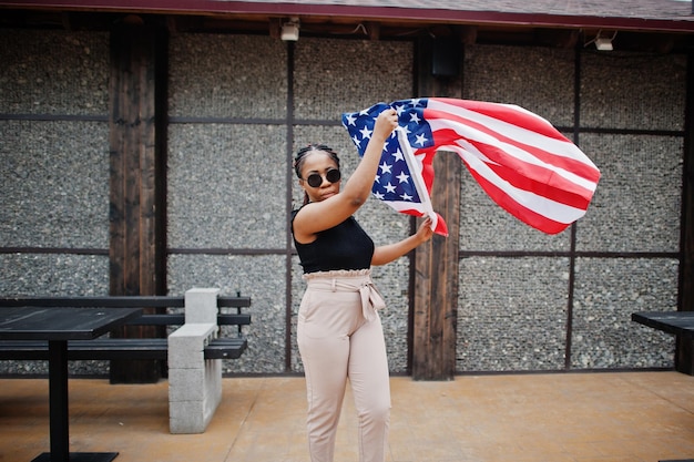 Elegante mujer afroamericana en gafas de sol posó al aire libre con la bandera de estados unidos