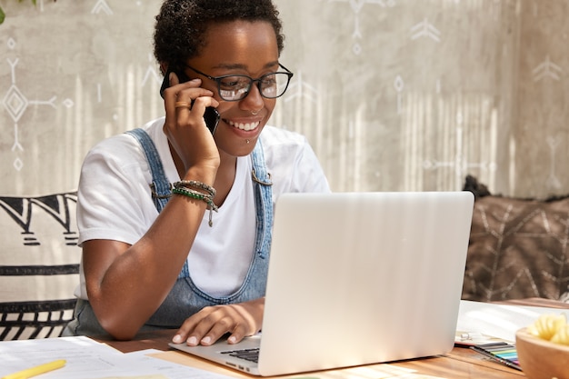 Elegante mujer afroamericana llama a miradas de teléfonos inteligentes en la computadora portátil, actualiza el software