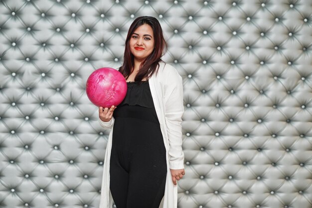 Elegante mujer asiática con bola de boliche rosa en la mano contra el fondo de la pared plateada