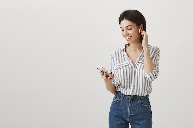 Elegante mujer atractiva sosteniendo teléfono móvil y escuchando música con auriculares inalámbricos