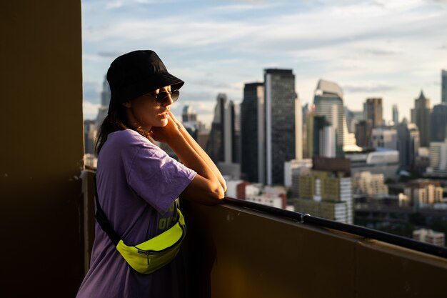 Elegante mujer caucásica en panamá de moda y bolso de neón de cintura en el techo en Bangkok