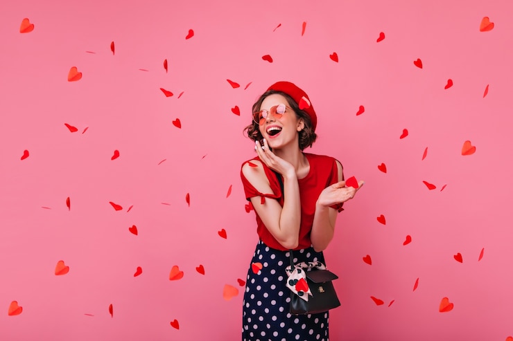 Foto gratuito elegante mujer despreocupada posando en el día de san valentín. riendo a chica rizada glamorosa en boina de pie bajo confeti rojo.