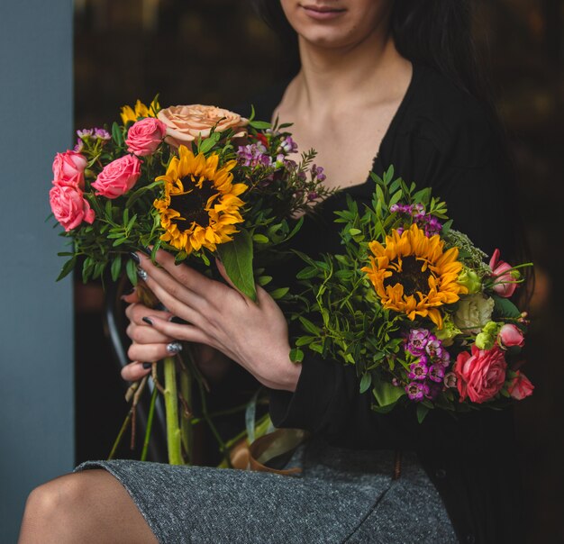 Una elegante mujer con dos ramo de rosas y girasoles