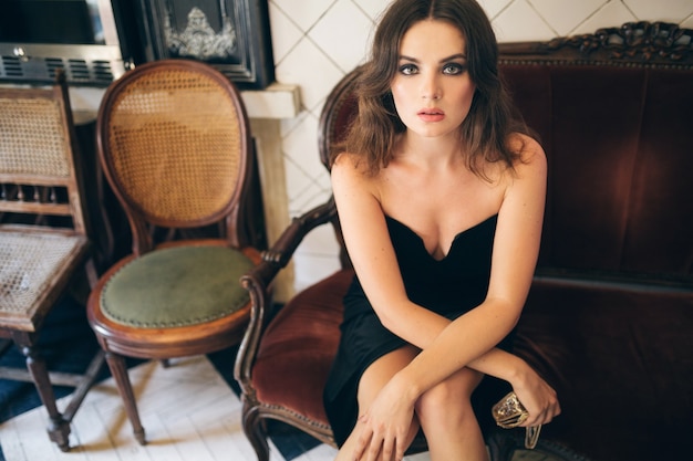 Elegante mujer hermosa sentada en un café vintage con vestido de terciopelo negro, vestido de noche, dama elegante rica, tendencia de moda elegante, mirada seductora sexy, figura flaca atractiva